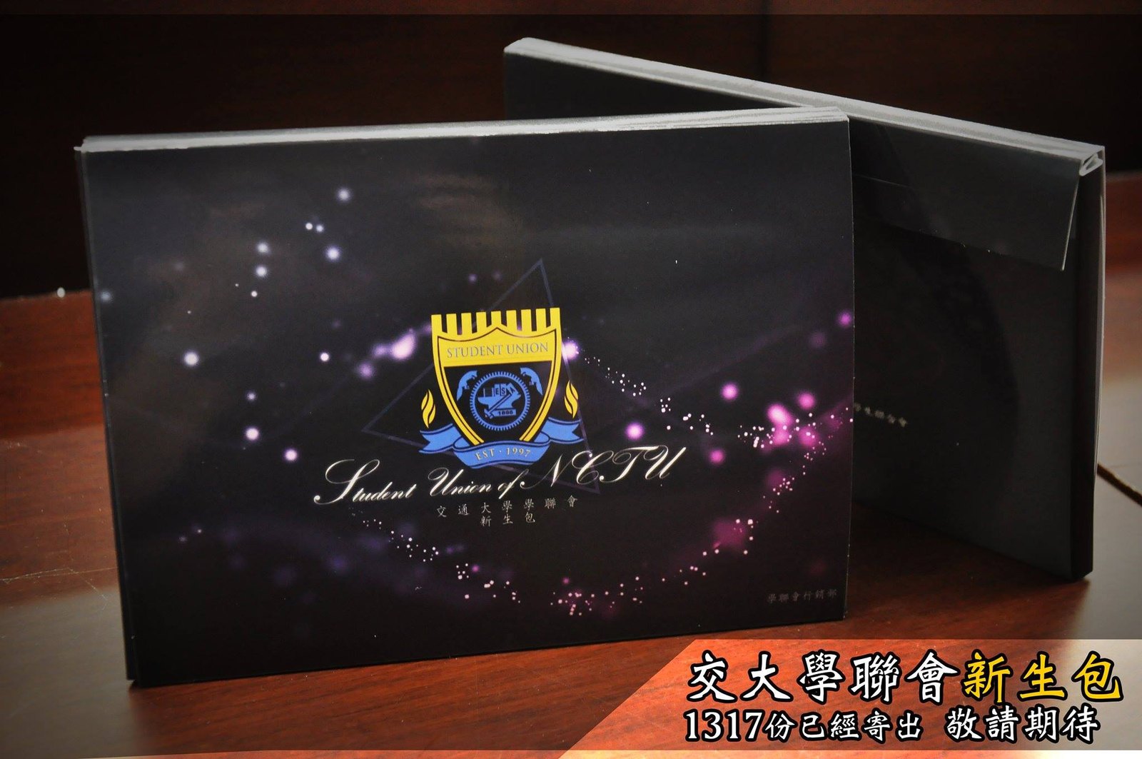 深色盒子的照片,盒面有徽章,右下角寫交大學聯會新生包 1317 份已寄出 敬請期待